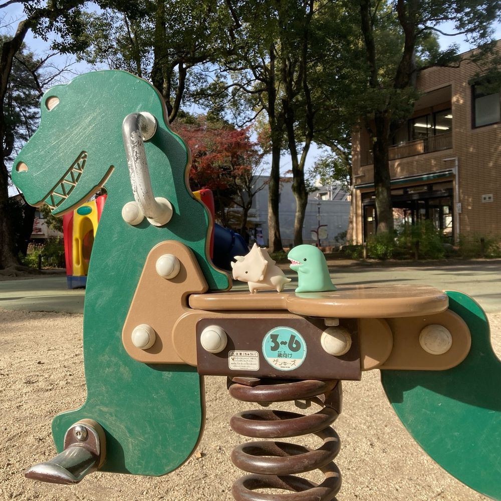 恐竜型のバネ遊具の上に乗る、ソフビ製のトリケラトプスとティラノサウルス