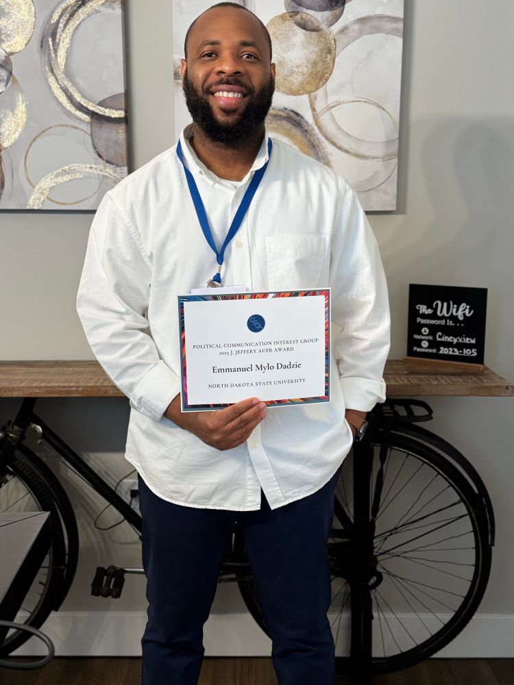 Emmanuel Mylo Dadzie, wearing a white dress shirt, holding an award certificate 