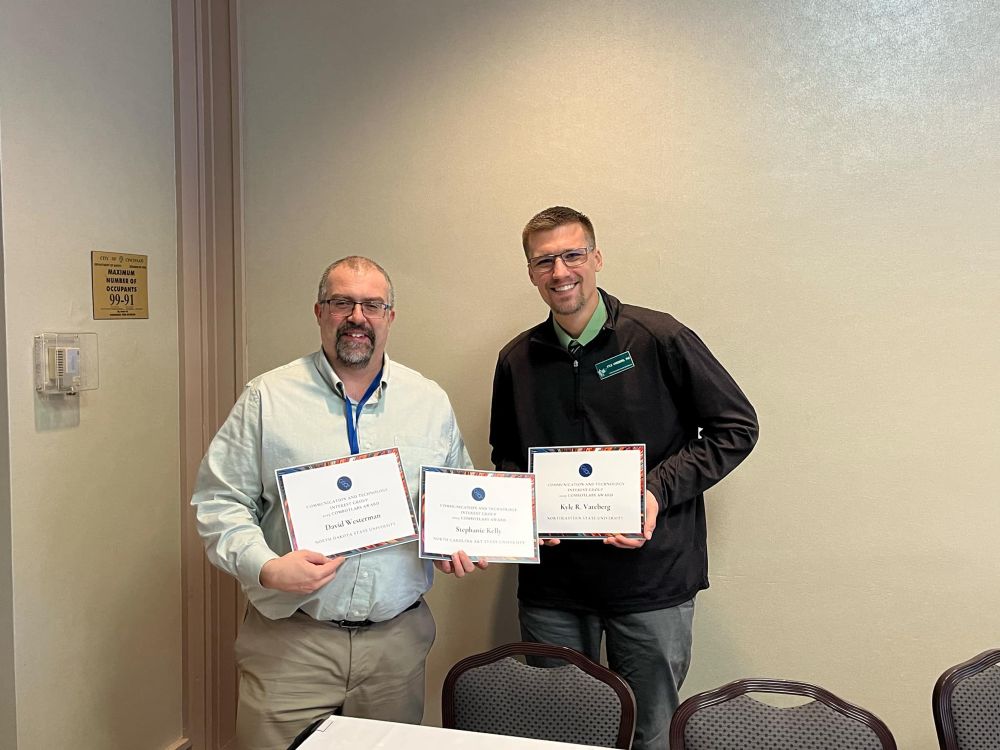Two men holding three award certificates 