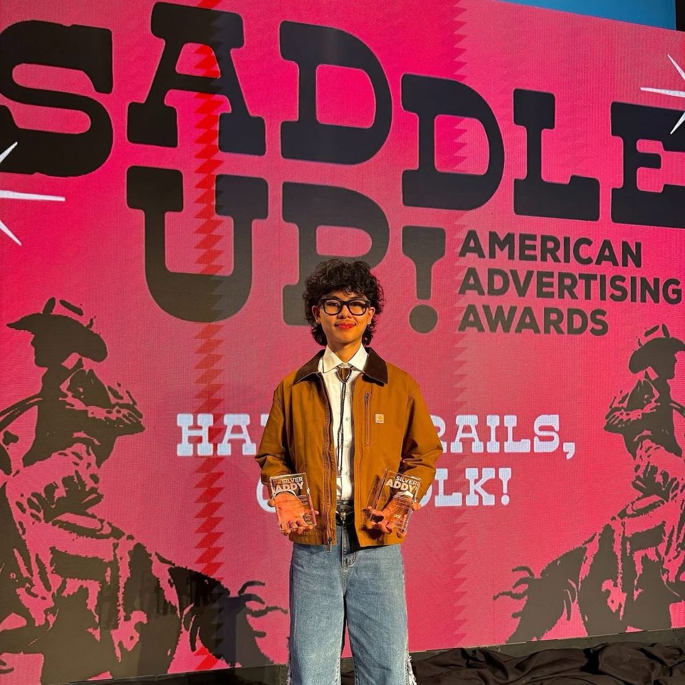 Xyle Altura standing in front of a banner that says "Saddle Up! American Advertising Awards"