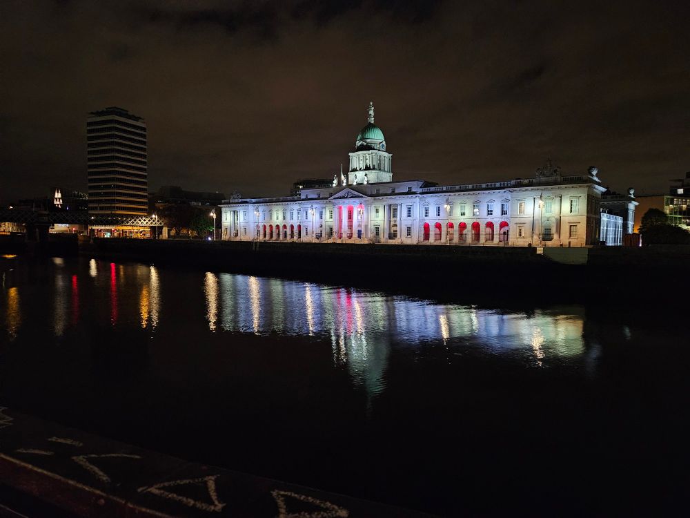 Dublin Customs House building lit by different colours and reflected by the River Liffey in the middle of the night. 