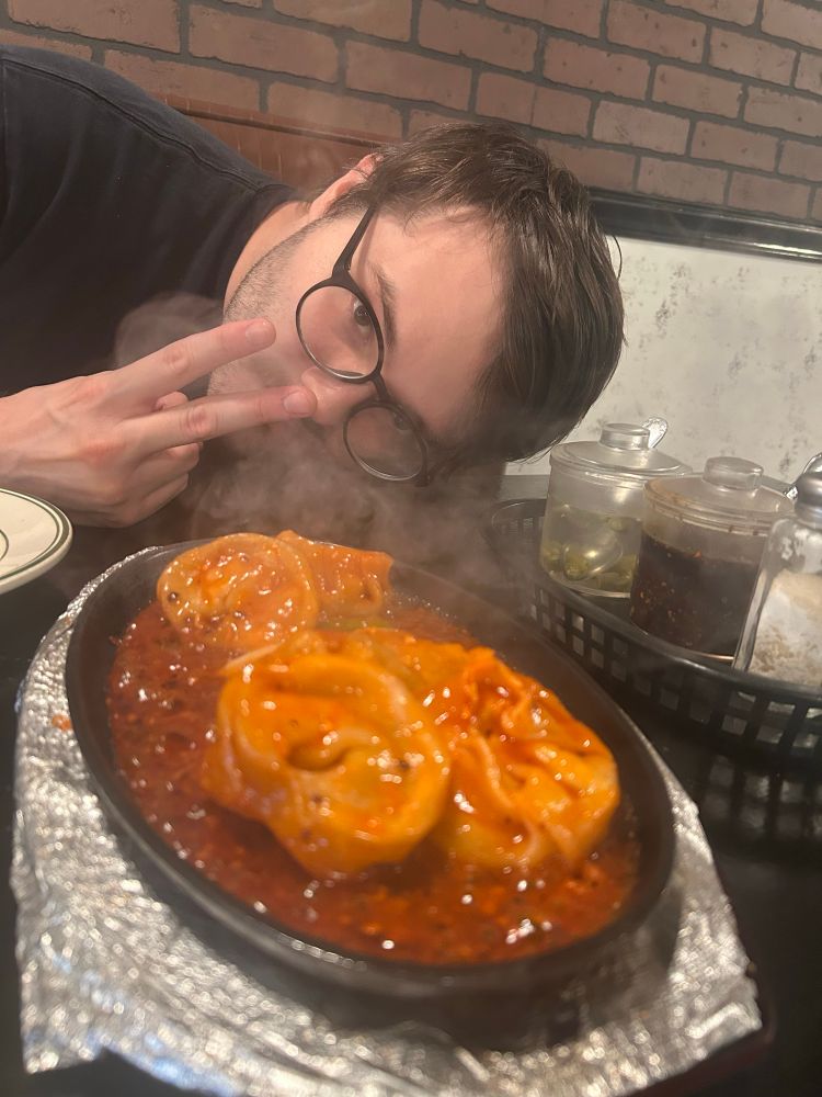 Sizzling vegetable dumpling platter with Ru’s partner throwing a peace sign in the background