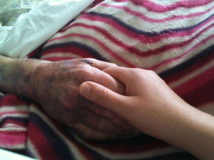 A photo of two people holding hands. One hand is bruised and purple, the other not. There's a pink striped fleece blanket in the background. 