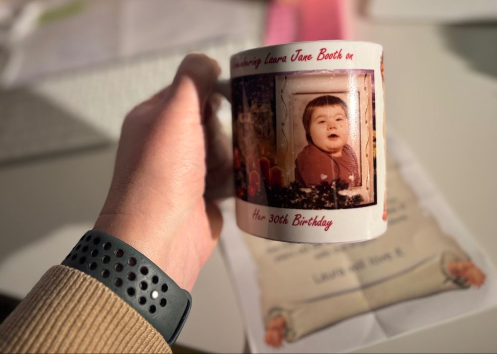 A hand holing a mug with a photo of an 8 year old child in a red jumper on it. The text reads Remembering Laura Jane Booth on her 30th birthday