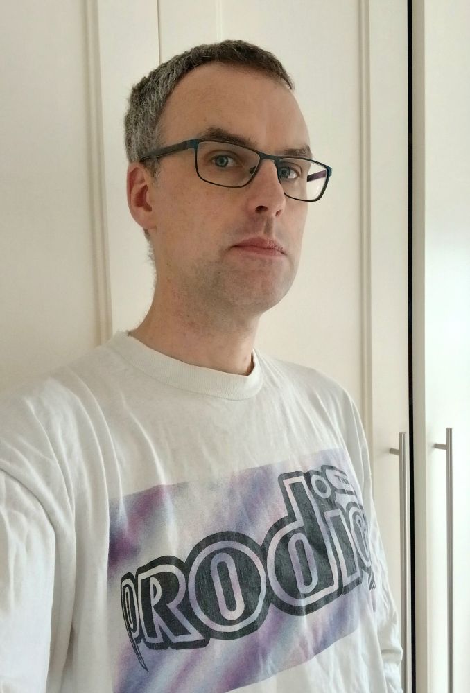 A selfie of a greying middle-aged man, his tired appearance offset by an extremely fetching (and authentic) long sleeve white t-shirt bearing the Music for the Jilted Generation-era Prodigy logo