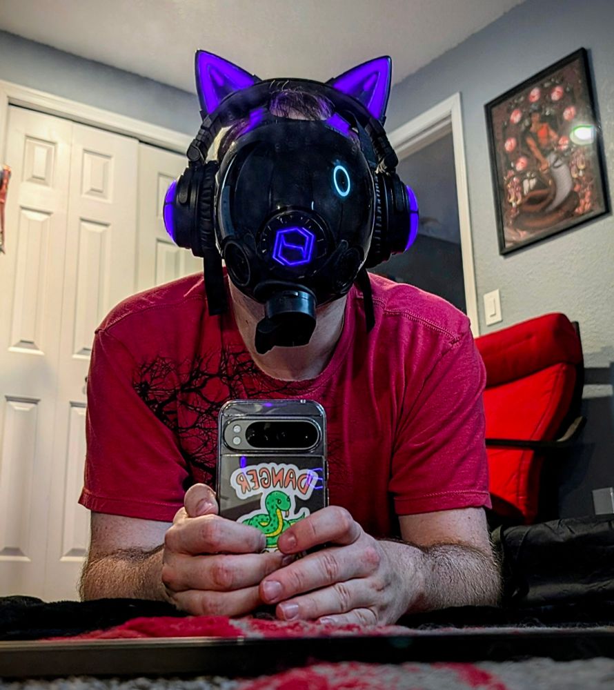 Me wearing a gas mask with hex corp logo, light up cat headphones, and normal clothes, laying down in front of a mirror.
