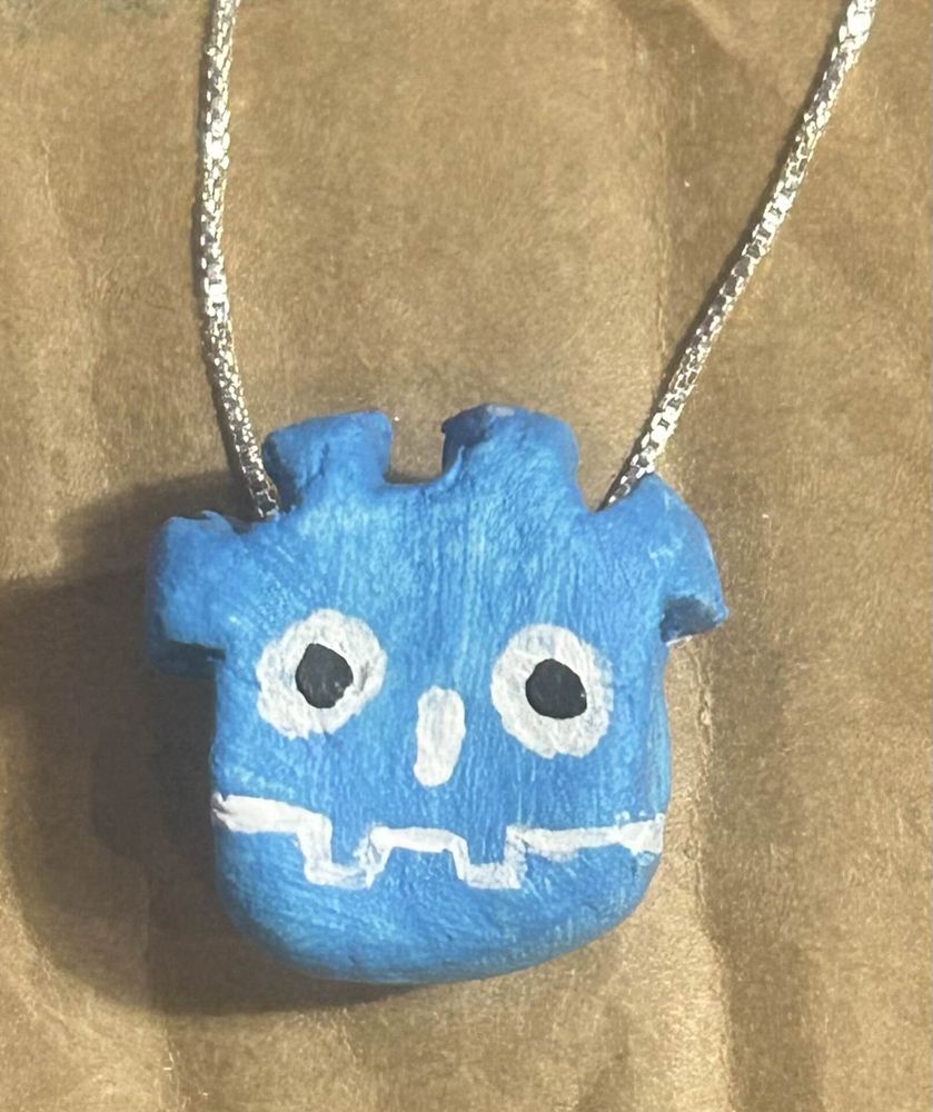 A picture showing a diy necklace of the godot mascot/logo made of clay and paint. a necklace chain is attached to it