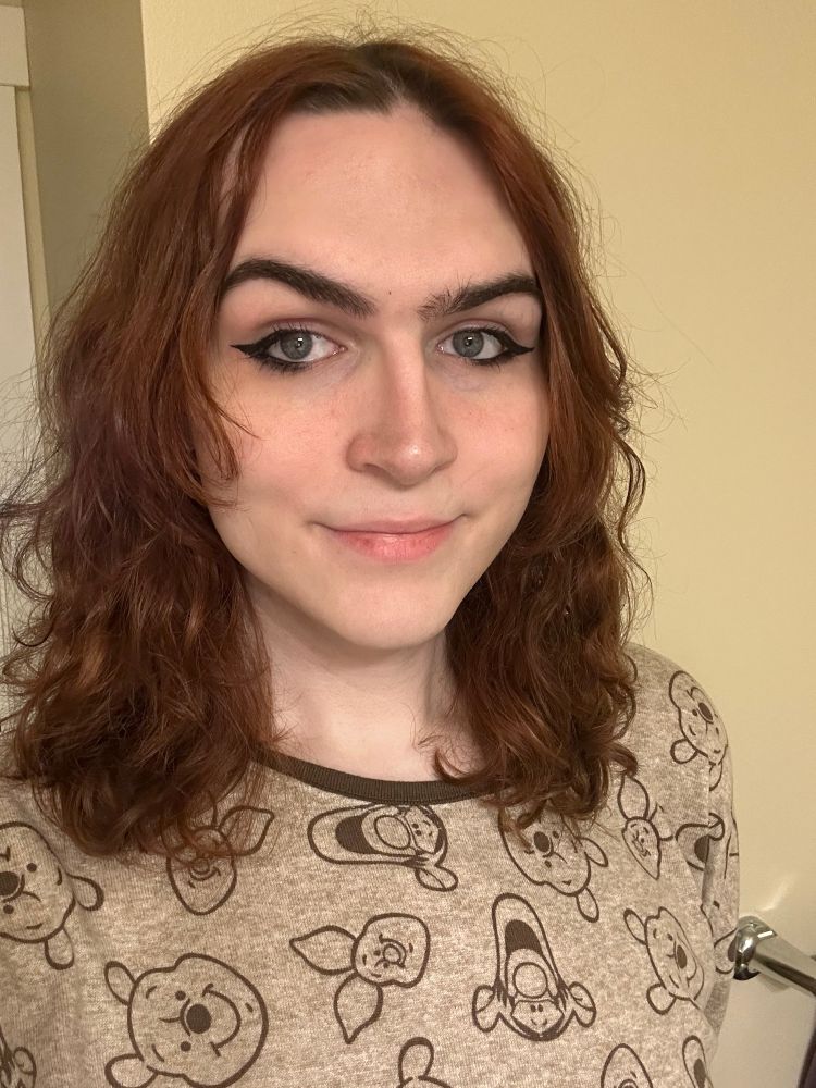 a selfie of me from the shoulders up. I'm doing a slight smile into the camera. i'm wearing black winged eyeliner slightly smoked out on the lower lashline and i'm wearing winnie the pooh pajamas