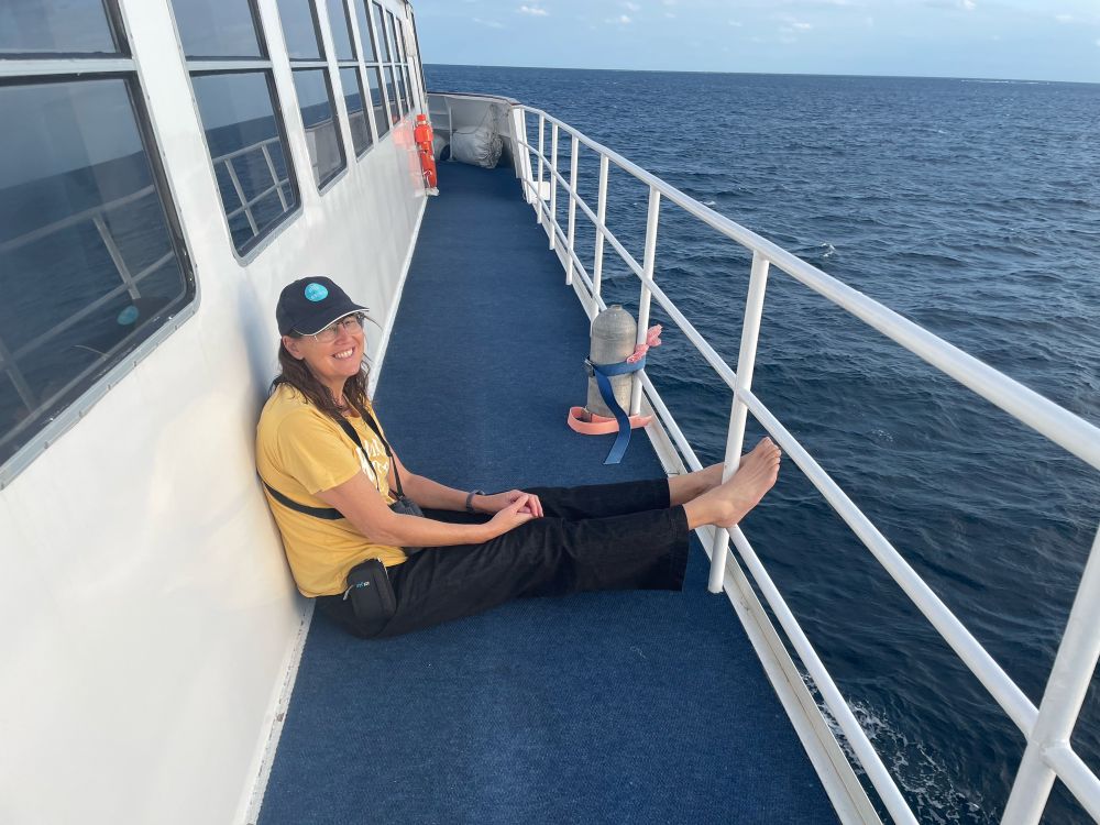 Me in yellow shirt sitting on the deck of a diving boat headed to Ribbon Reefs, Great Barrier Reef on holiday to enjoy the ocean I research- my binoculars with harness are my constant companion 