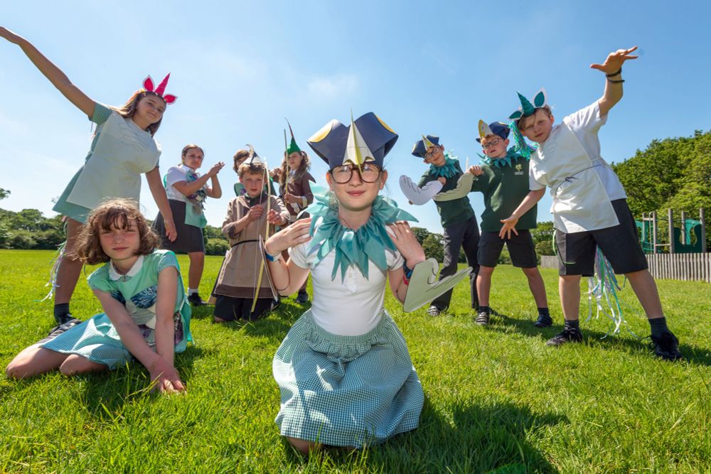 Group of children in blue and white costumes and headdresses performing outdoors on a grassy field in the sun
