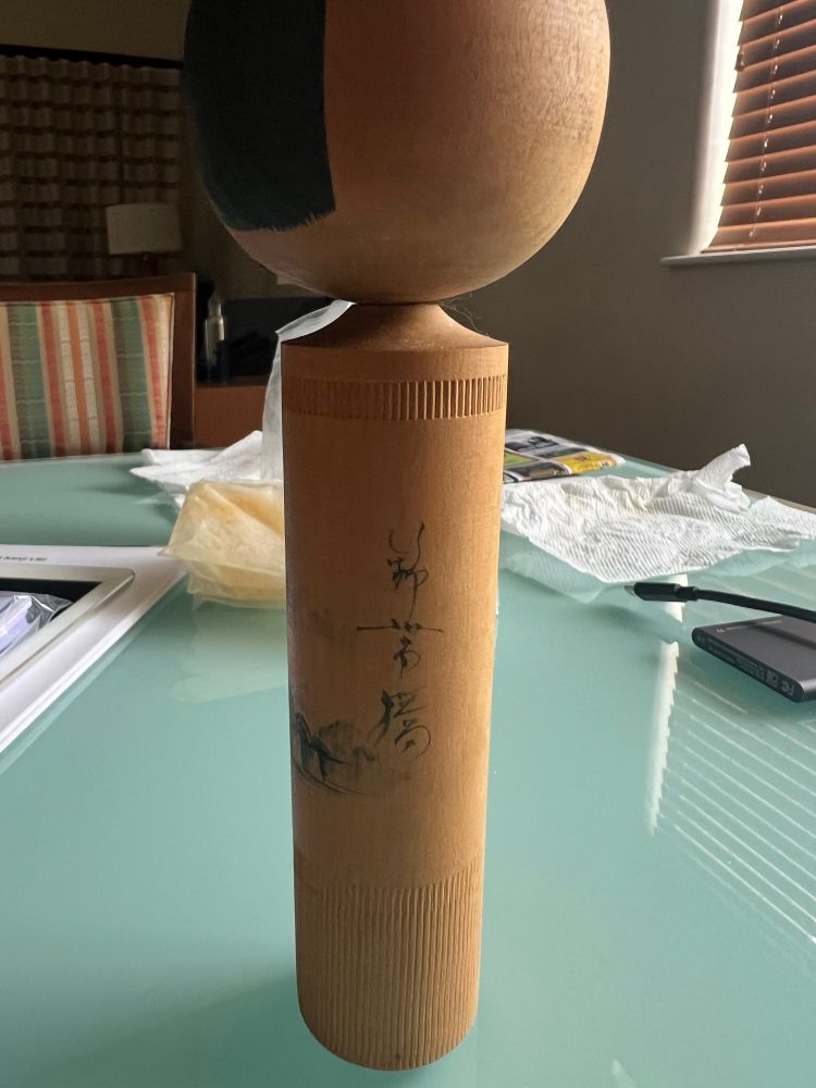 The side view of a kokeshi doll obtained in Kaleakekua, Big Island, Hawaii. The creator’s signature features prominently on the side, where it is typically located on the bottom.