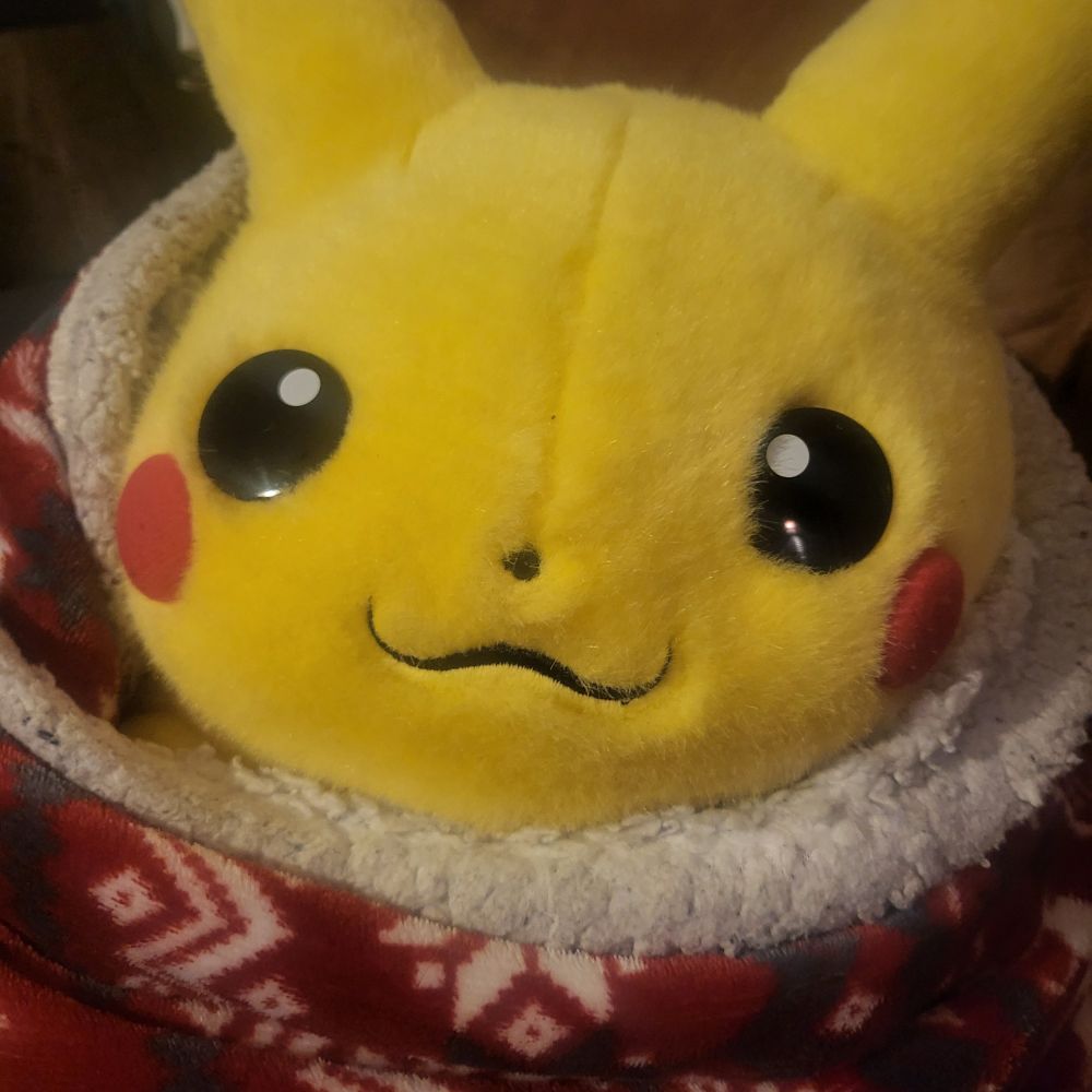 A 1999 Tomy Hasbro Jumbo Pikachu stuffed animal, snuggled up and cozy in a red and white Christmas themed blanket, with snowflake and reindeer imagery