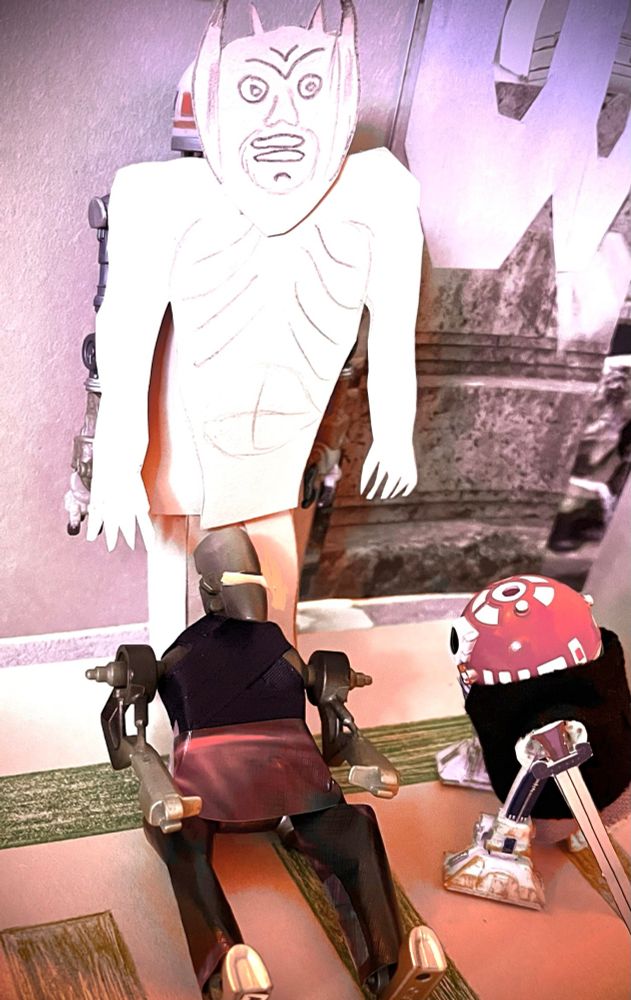 B: Interior, Angelus’ Mansion, in front of MA-13 as Acathla still but now the lighting is white and rosy. And sprawled below Acathla now is Archy as Angel! His eye slit is glowing yellow. R3-T2 as Buffy is right of him, sword now down, is staring at him intently. 