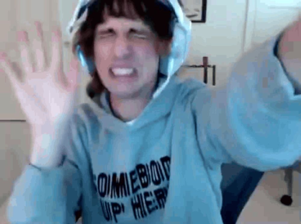 a man wearing a hoodie and headphones is making a funny face with his arms in the air .