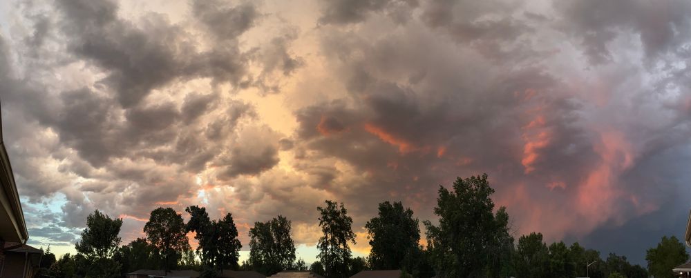 Panoramic photo of the sky before sunset with orange and pink colors dancing off the clouds with dark stormy sky to the east 