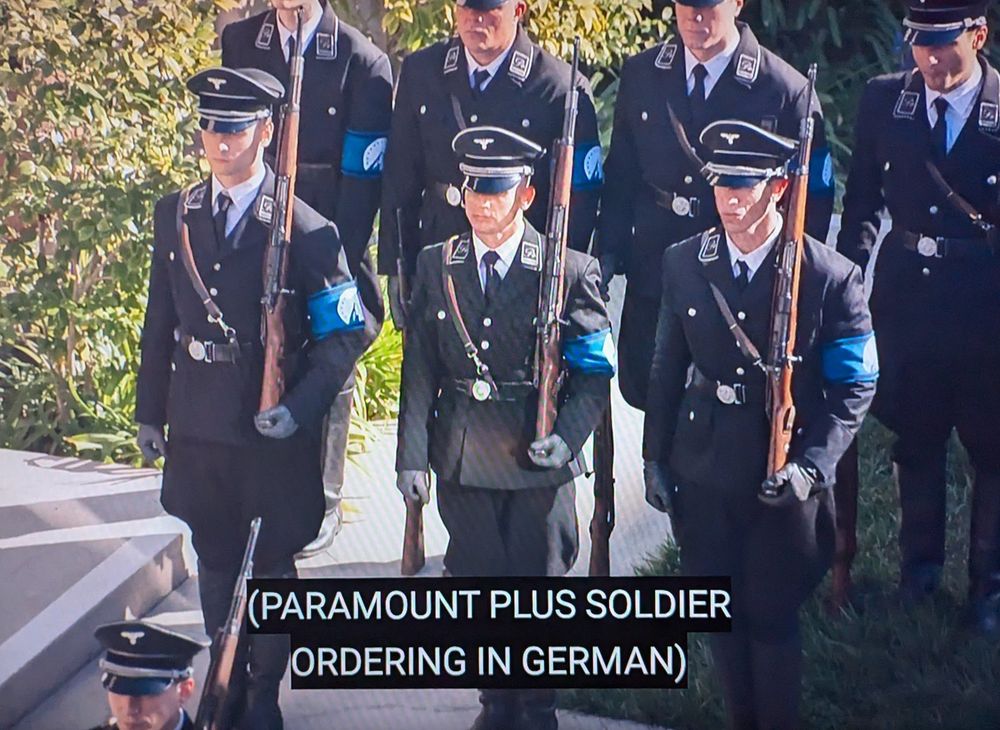 Scene from The Rehearsal season 2 with marching naxi-esque soldiers wearing paramount plus blue armbands.