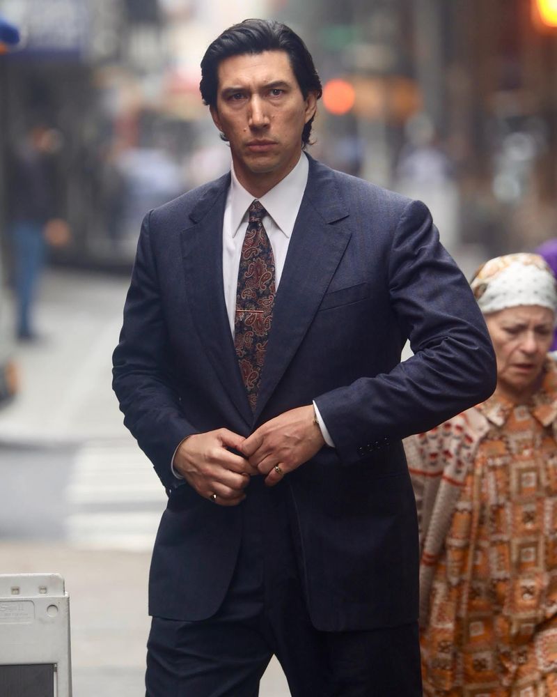 adam driver dressed in a dark blue suit with short hair and wearing 2 pinky rings