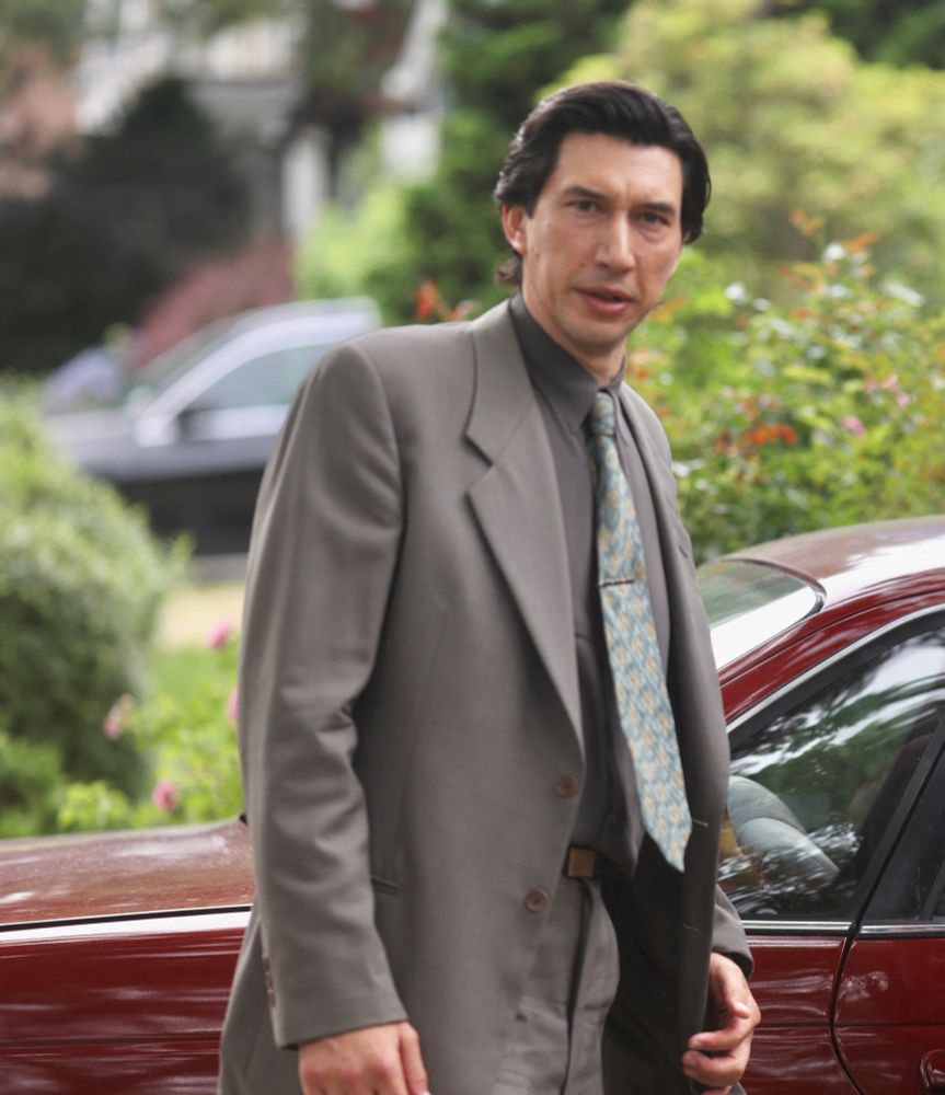 adam driver wearing a grey suit standing in front of a red car on the set of Paper Tiger