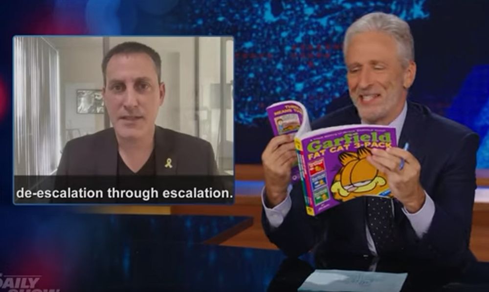 Jon Steward, silver haired and lightly bearded wearing a dark blue, almost violet in the lighting suit, on The Daily Show, showing an Israeli Gov't representative(?) declaring that their official strategy re: the genocide in Gaza/West Bank and potential war with Lebannon is "de-escalation through escalation", and holding up a Garfield the Cat Omnibus (Fat Cat 3 pack, vols 7-9 I think?) collection trying to find an example of such double speak, after already having held up copies of Orwell's 1984 and Cathy O'Neill's Weapons of Math Destruction.