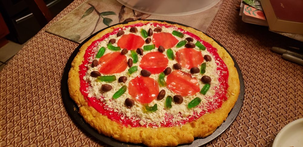 Cookie cake decorated with frosting, shaved white almond bark, milk duds and gummies to look like pizza 