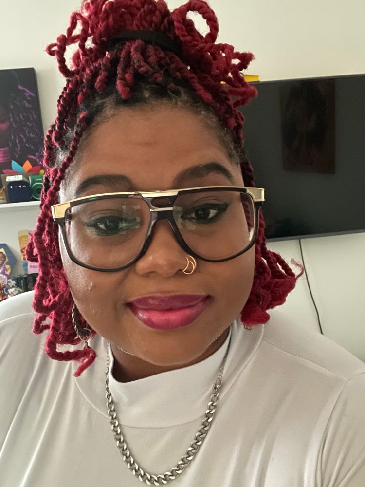 Black woman with glasses and red two strand twists. White shirt and silver necklace 