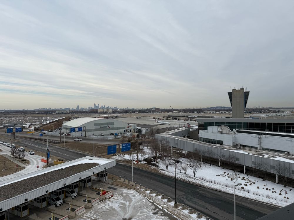 The Philadelphia skyline from a high vantage point. Taken from PHL airport during an overcast day. Snow is on the ground, though old snow, and the clouds have a lower ceiling with a wispy effect - though total overcast. Light lavender hues with a slight tinge to orange in the distance. Taken and shared to communicate and evoke empathy in that homey feeling in the heart when you arrive in your comfort zone. 