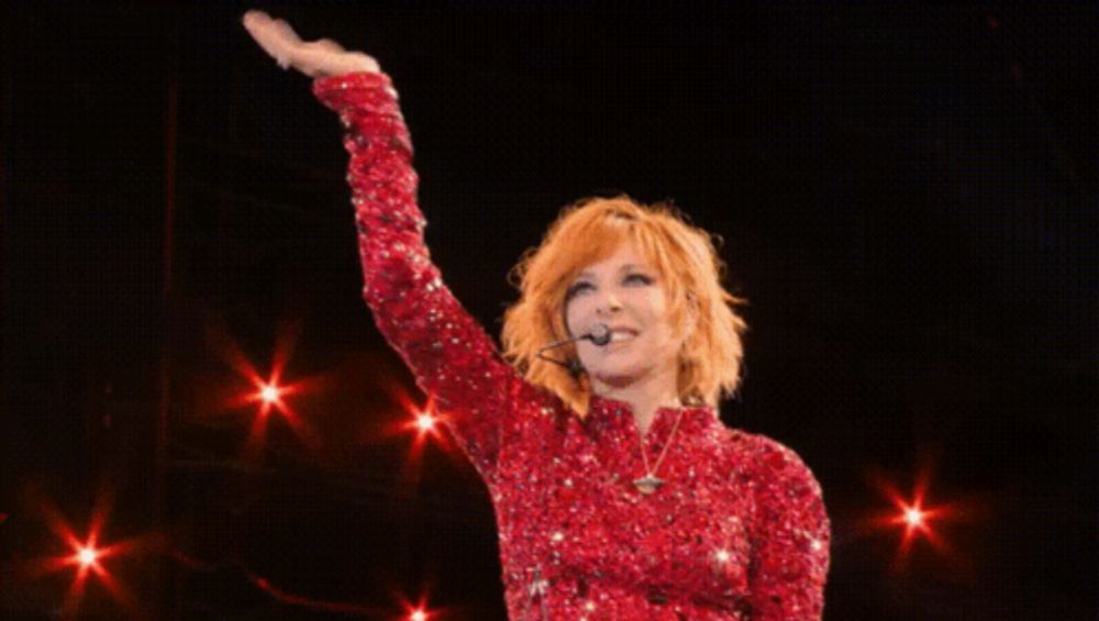 a woman in a red sequined dress is singing into a microphone on stage