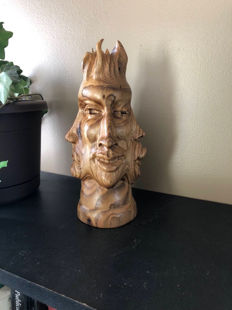 sculpture in butternut depicting 4 faces that share an eye, cheek, neck, brow, and hair. 