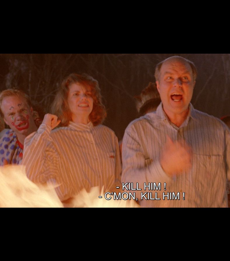 From the film Ernest Scared Stupid. A suburban white couple in matching button-downs and one clown shout "KILL HIM! C'MON KILL HIM!" behind some flames.