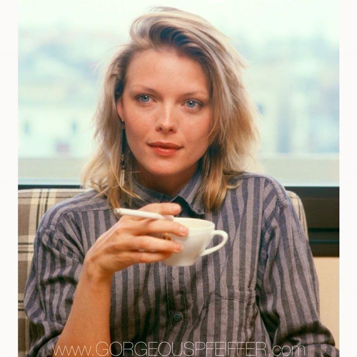 Michelle Pfeiffer in 1985 (according to alamy) in a buttoned up Black & Grey striped shirt, tousled blonde hair, holding a cigarette and a coffee mug in her right hand
