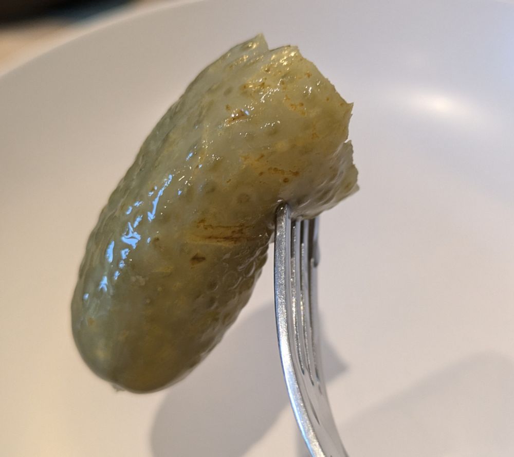 Photo d'un gros cornichon aigre doux a moitié croqué, planté sur une fourchette