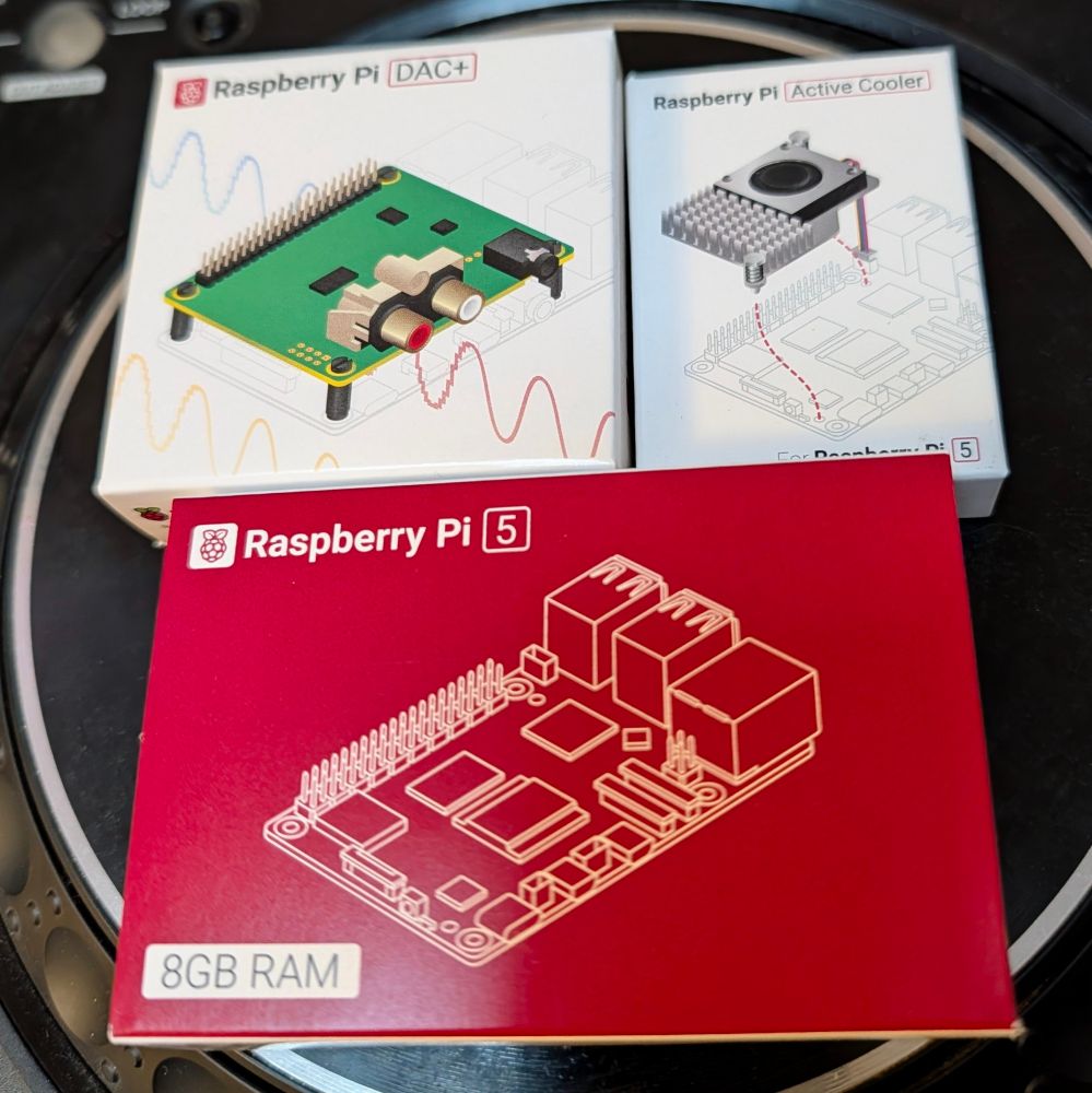 a raspberry pi 5 with 8 GB ram, an audio card for the pi, and a cooler, all in their boxes, placed on top of a DJ player jog wheel 