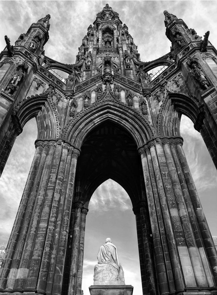 Black and white photo of the monument to Sir Walter Scott on Princes Street in Edinburgh. Tall, ornate, gothic arches with intricate carved stone details stretch over him to give shelter. 