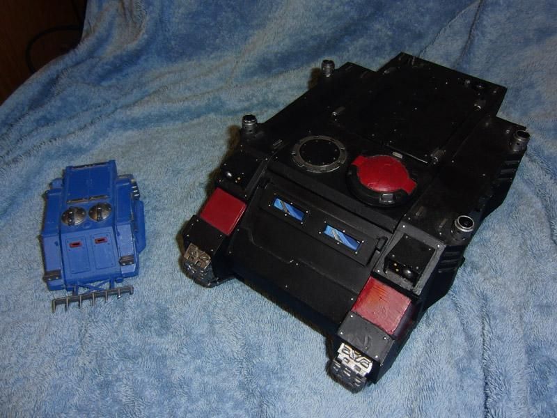 Photograph of a 28mm scale MkI Rhino APC in Ultramarines Blue being dwarfed by a scratchbuilt 54mm scale Mk2 Rhino.