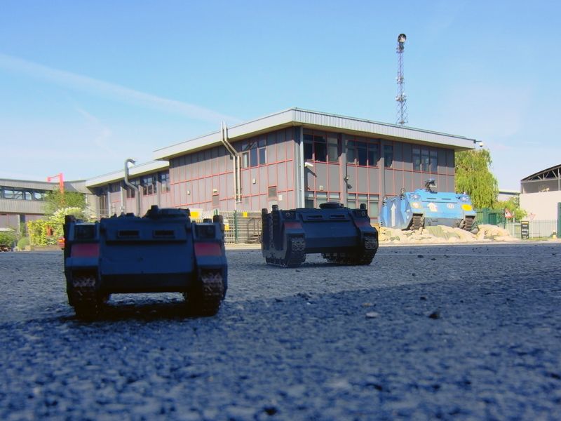 Photograph from outside Warhammer World. The perspective has been set up to try to make a 28mm scale, 54mm scale and the full-size Rhino look like they're all part of the same mechanised advance across the car park.