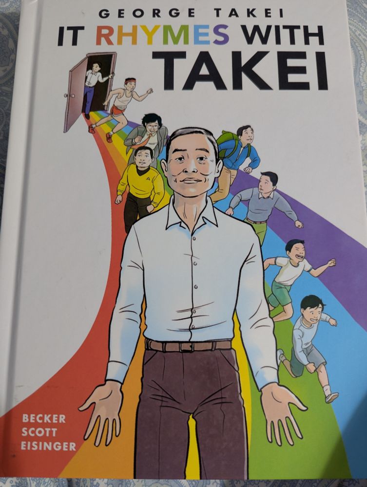 The book cover of "It Rhymes with Takei." An illustration of a door in back with versions of George throughout his life running out of it, on a rainbow-colored path. Adult George is standing in front, wearing brown pants and a white shirt.
