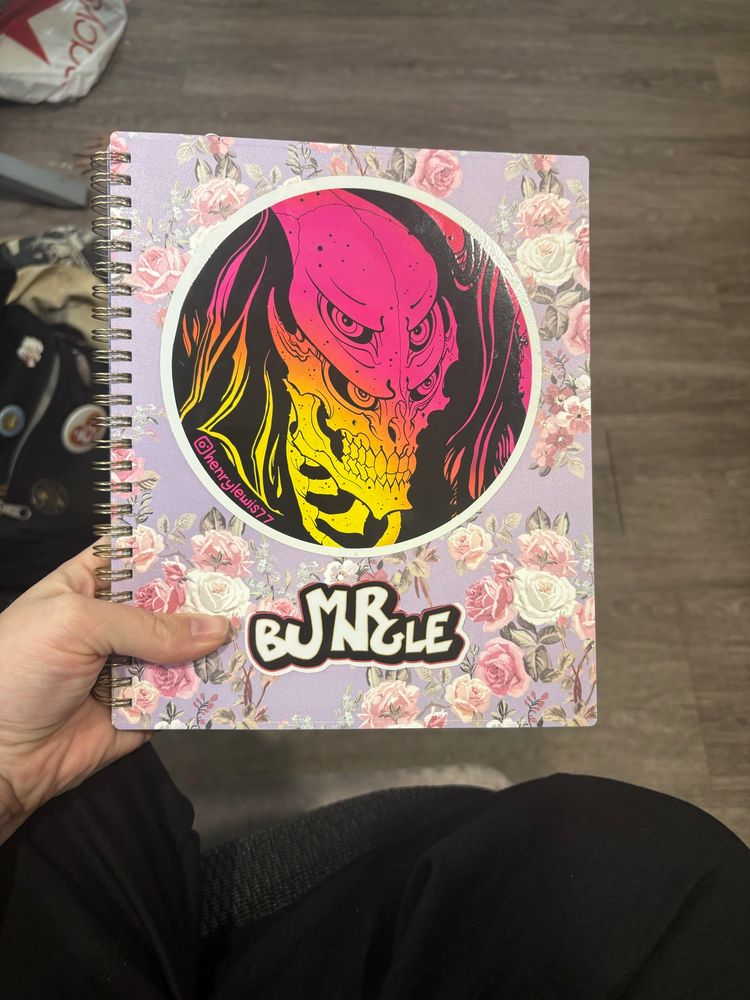 Academic-style planner with a sticker of a monster that looks like predator drawn by Henry Lewis, and a Mr. Bungle sticker below it”