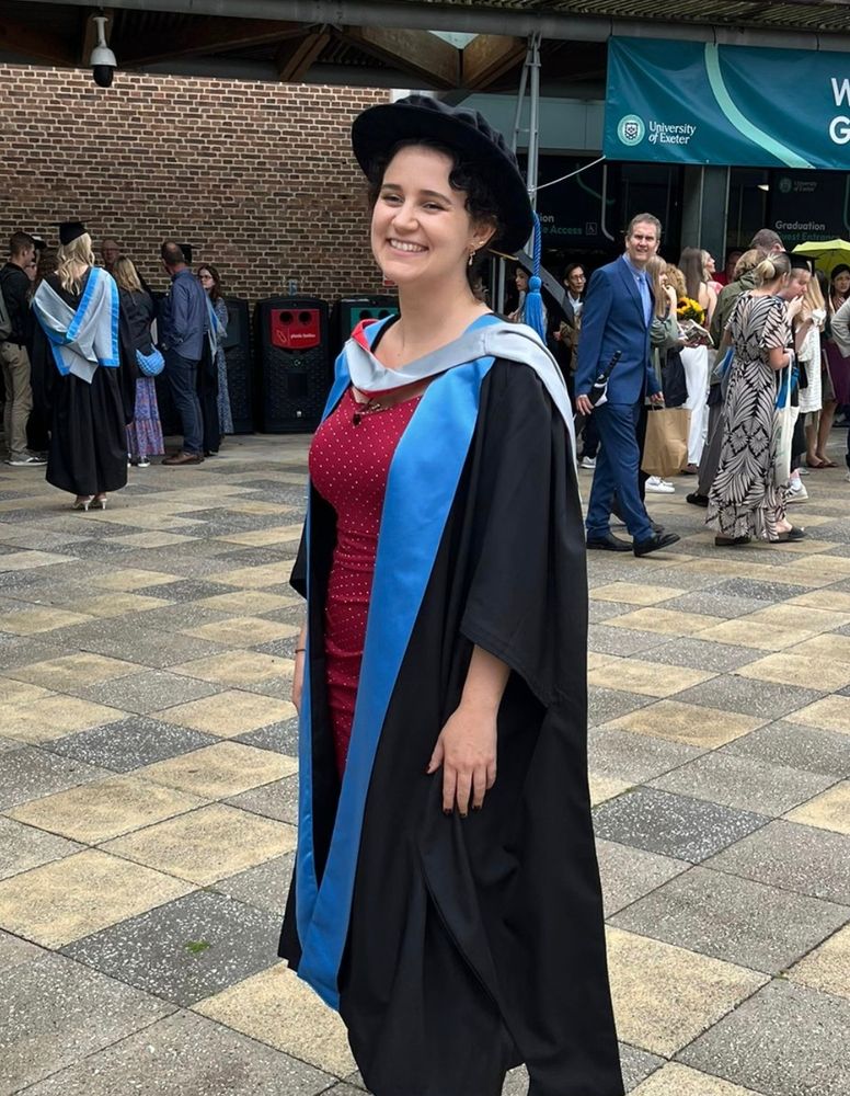 Rebekah outside in red dress and graduation robes. She is smiling and there is a crowd behind her.