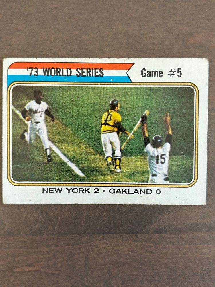 Card depicting Game 5 of 1973 World Series. Cleon Jones is running into score. Jerry Grote has a bat in his hand. His arms are raised to tell Cleon he does not have to slide. Ray Fosse is looking out towards right field as Jones is about to run behind him. 
