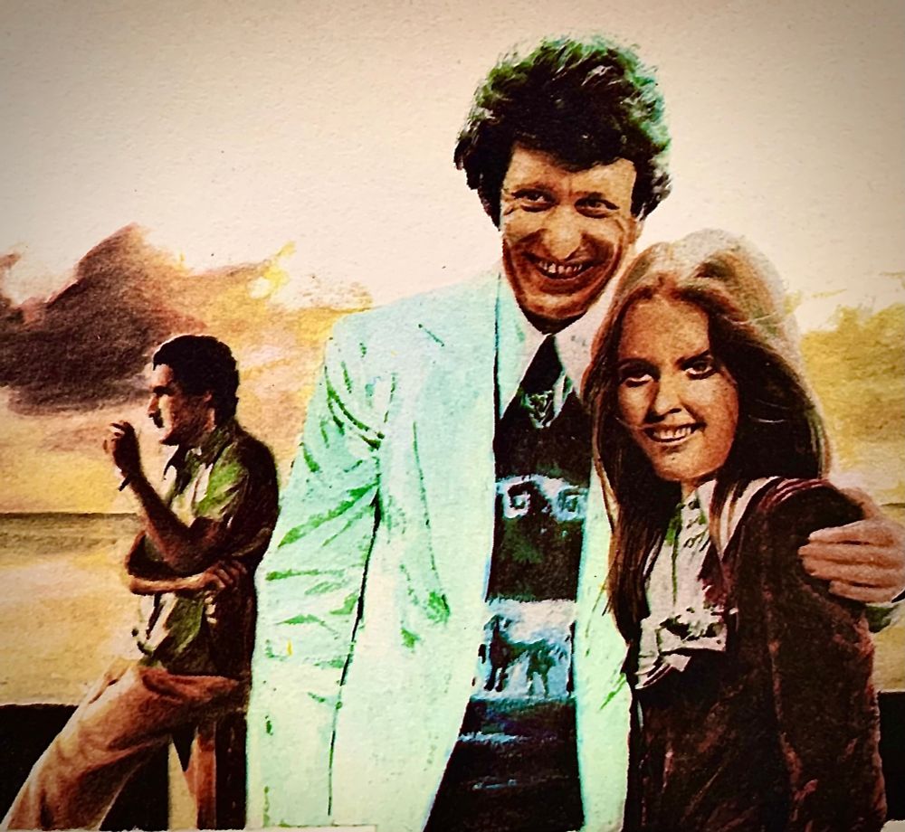 A man smoking in the distance whilst another man and a woman smile at the viewer