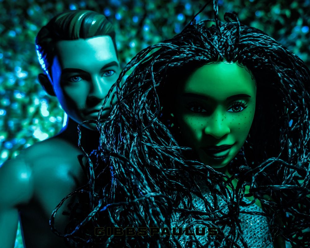 A white, male doll, and a green, female doll with braided hair, in a post-coital moment