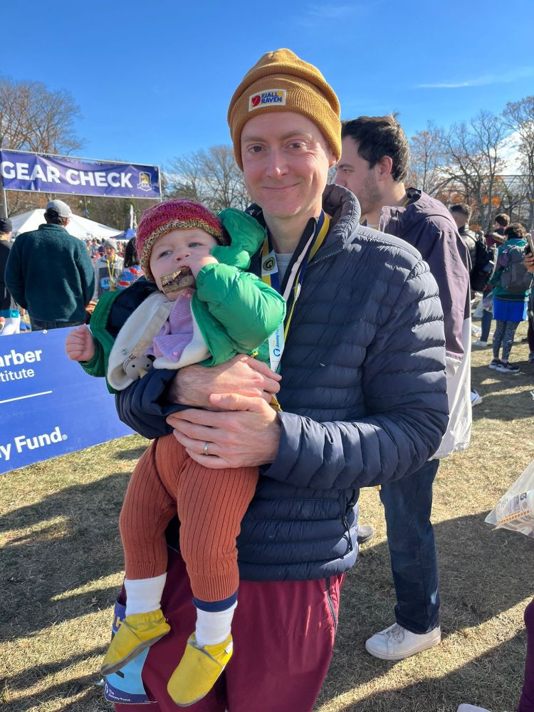 Runner holding his daughter while she eats a sandwich after a race.