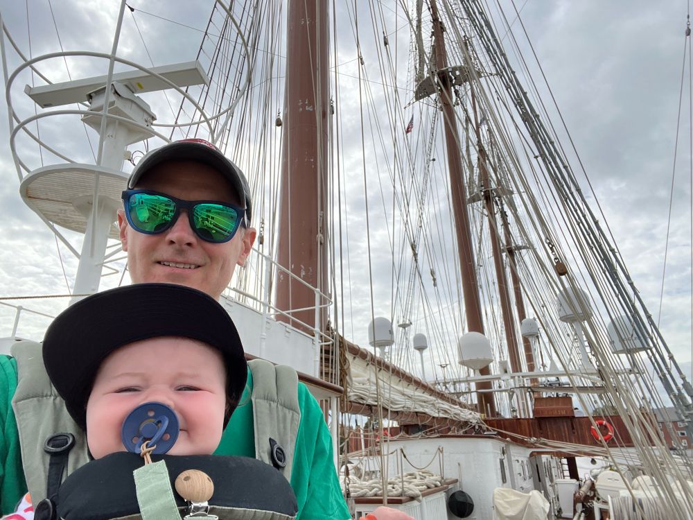 Man and baby in front of a large tall ship.