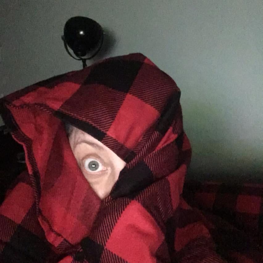 My head wrapped in a red Buffalo plaid blanket, with only one eye exposed looking at the camera.