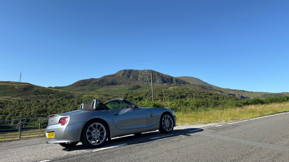 Silver BMW Z4 convertible with roof down parked at the side of a road in North Wales with Moel Llechwedd in the background