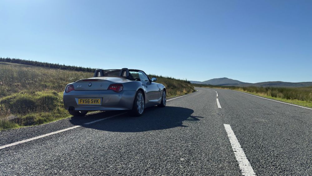 Silver BMW Z4 convertible with roof down parked at the side of a road in North Wales in the background