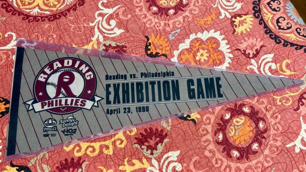 Grey pennant that says Reading vs. Philadelphia and Exhibition Game (in the largest letters) and April 23, 1990. It has a maroon Reading Phillies logo and small ads for Pringles, Sunny Delight, etc.
