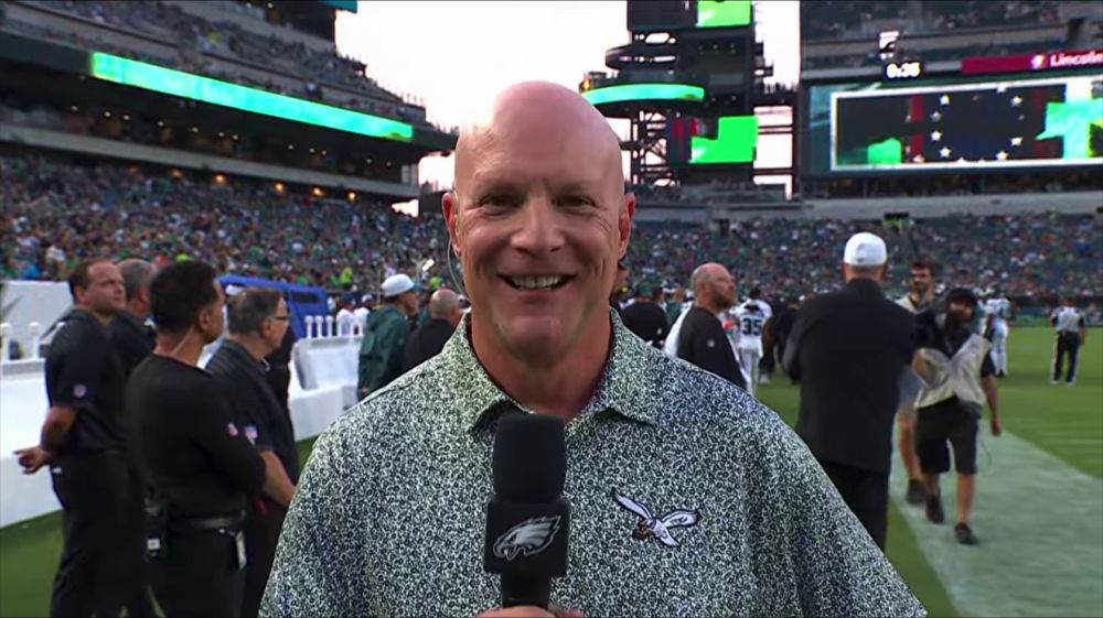 Dave Spadaro, Eagles team reporter, holding an Eagles microphone and in a green and white… speckled? polo. It has the 1980s Eagles logo on it.