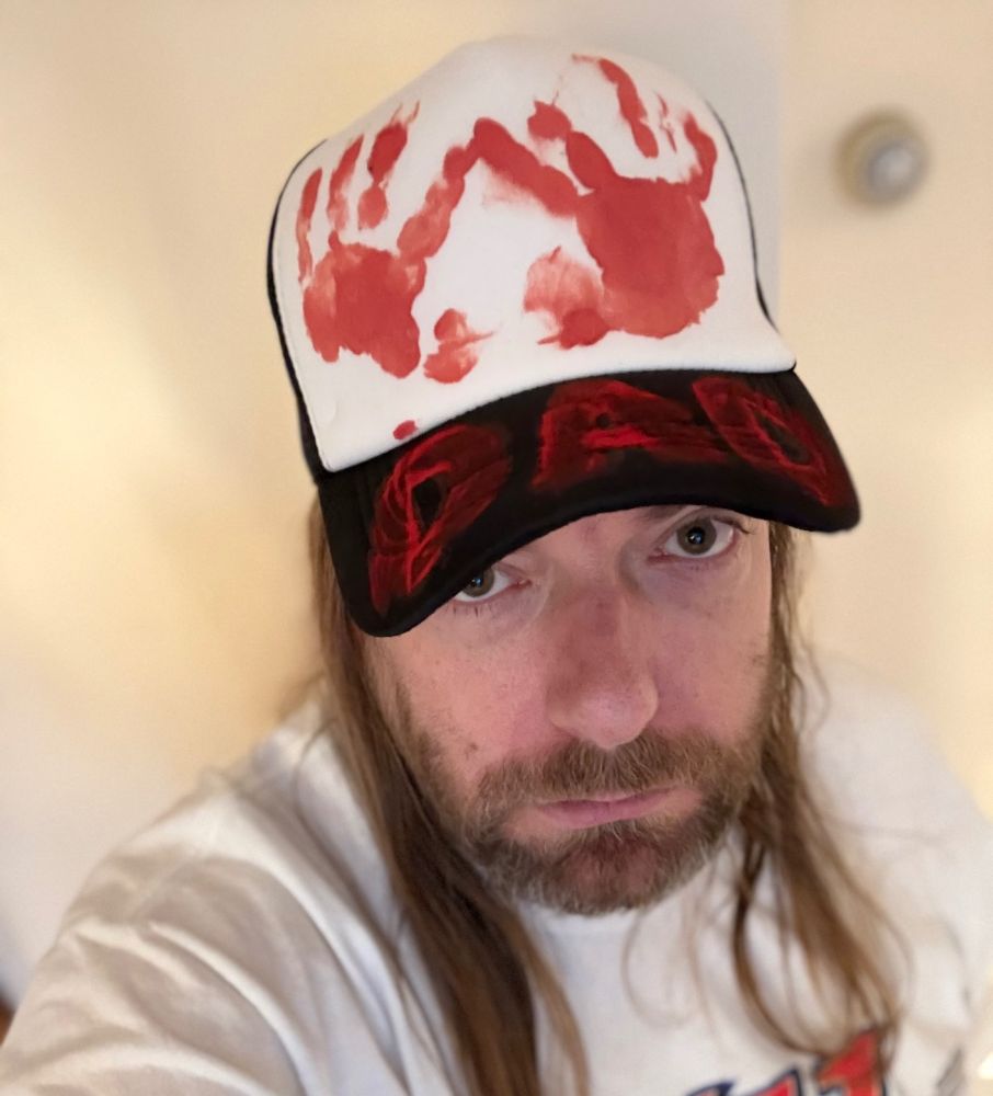 Selfie of Dan. He has a White Jesus look. Ooh, isn’t he handsome! He’s wearing a black and white trucker hat with his son’s handprints in red on the top and “DAD” on the brim.