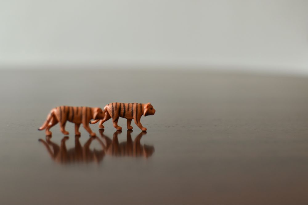Two toy tigers on a brown surface